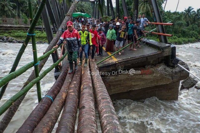 Bupati Bolmong Selatan Iskandar Kamaru menyeberangi jembatan darurat yang terbuat dari batang kayu kelapa. Bolsel kembali mengalami bencana banjir bandang pada Sabtu (1/8). (Foto: Dinas Kominfo Kabupaten Bolsel)