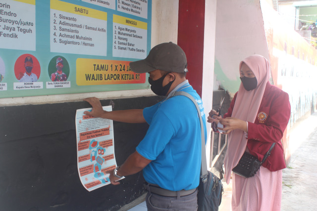 Anggota tim KKN 56 UMM bersama Kepala Dusun menempelkan poster edukasi.