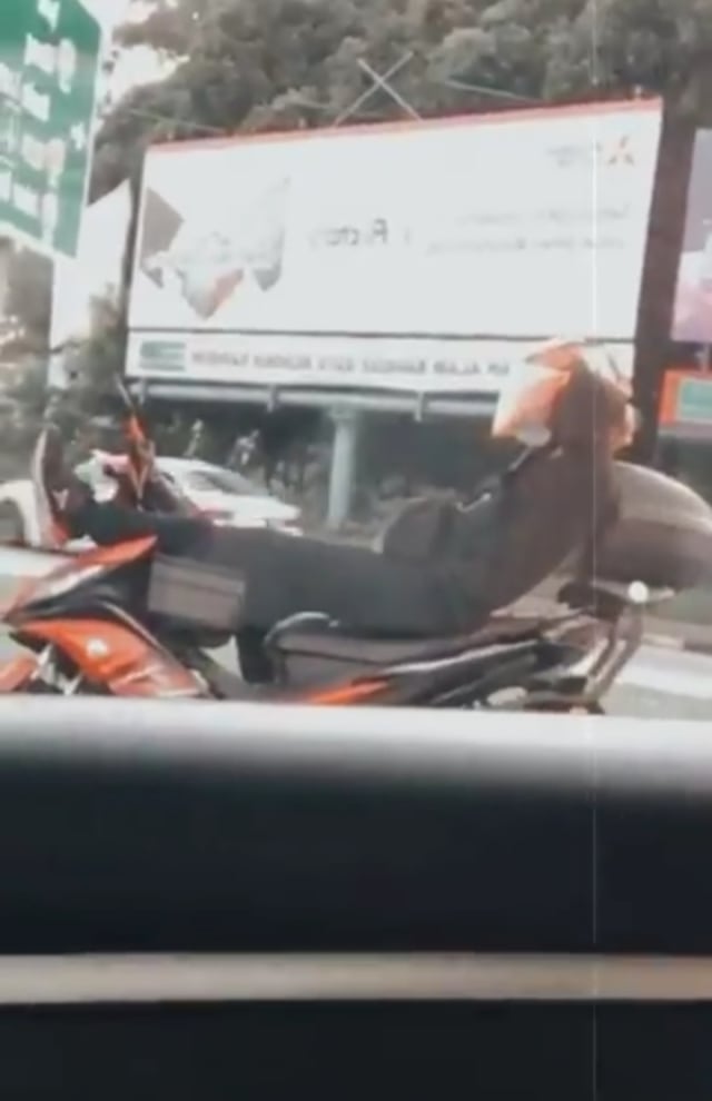 Momen kocak pengendara motor di Selangor, Malaysia,  sambil tiduran di atas motor saat menunggu lampu lalu lintas. (Foto: Twitter/Tangkapan Layar @izatiesyazlinaa) 