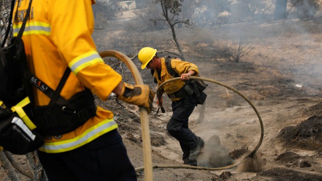 Pemadam kebakaran membawa selang air untuk memadamkan api yang masih tersisa pada kebakaran di Los Angeles. Foto: Patrick T. Fallon/ REUTERS