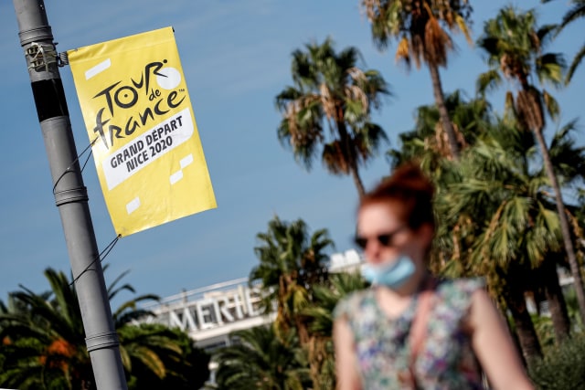 Seorang wanita memakai masker wajah berjalan melewati papan tanda menjelang Tour de France  Foto: STEPHANE MAHE/REUTERS