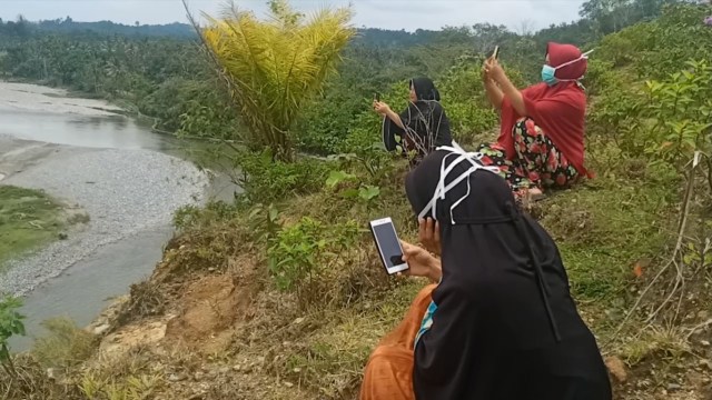 Mahasiswa di pedalaman Aceh Barat saat duduk di atas bukit pinggir sungai mencari akses jaringan internet untuk mengikuti proses belajar daring. Foto: Dok. acehkini