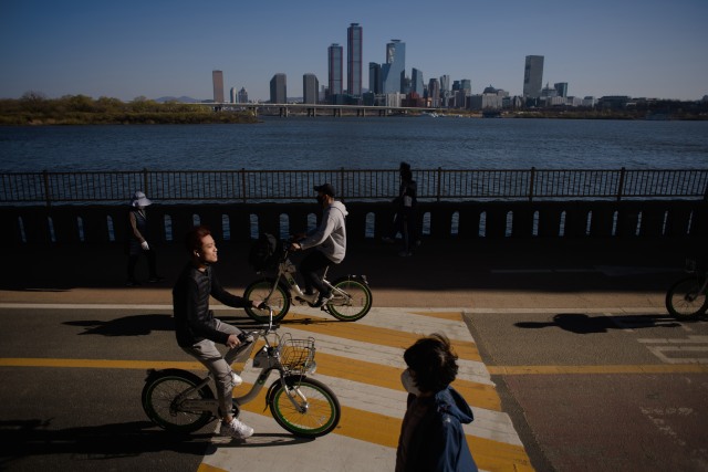 Pengendara sepeda dan pejalan kaki melewati sungai Han dan cakrawala kota Seoul. Foto: Ed Jones / AFP