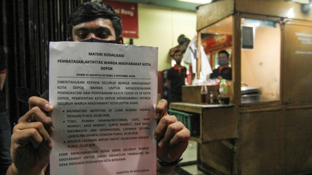 Pedagang menunjukkan lembaran sosialisasi pembatasan jam malam di margonda, Depok, Jawa Barat, Senin (31/8). Foto: Arif Firmansyah/ANTARA FOTO