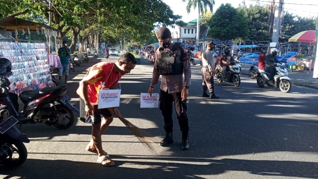 Seorang pengendara yang tak pakai masker diberikan sanksi sosial berupa menyapu jalan. Foto: Rizal Syam/cermat