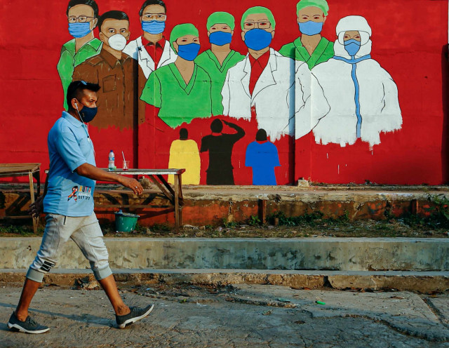 Warga yang menggunakan masker melintasi mural yang berisi pesan waspada penyebaran virus Corona di kawasan Tebet, Jakarta. Foto: Ajeng Dinar Ulfiana/Reuters