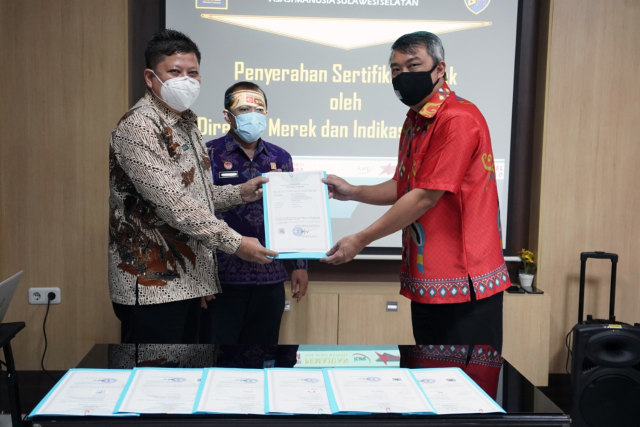 Direktur Merek dan Indikasi Geografis, Nofli (Kiri) menyerahkan 41 sertifikat merek secara simbolik kepada pelaku usaha di Sulawesi Selatan  yang berlangsung di Kantor Wilayah Kemenkumham Sulawesi Selatan. (Foto: Kemenkumham)
