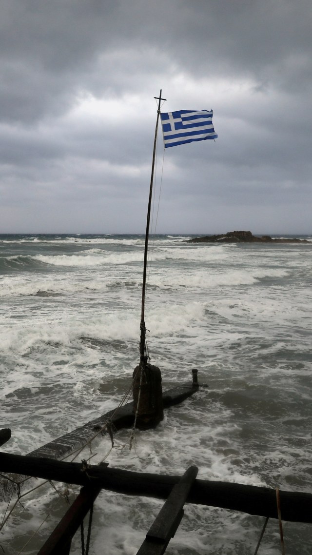 Bendera Yunani berkibar di pantai dekat kota Kyllini, saat badai langka, yang dikenal sebagai Mediterania, melanda Yunani barat, (18/9). Foto: Costas Baltas/REUTERS