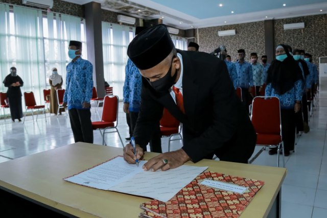 Pj Sekda Aceh Barat yang baru, Marhaban, menandatangani naskah pelantikan dirinya yang berlangsung via video conference. Foto: Dok. Pemkab Aceh Barat