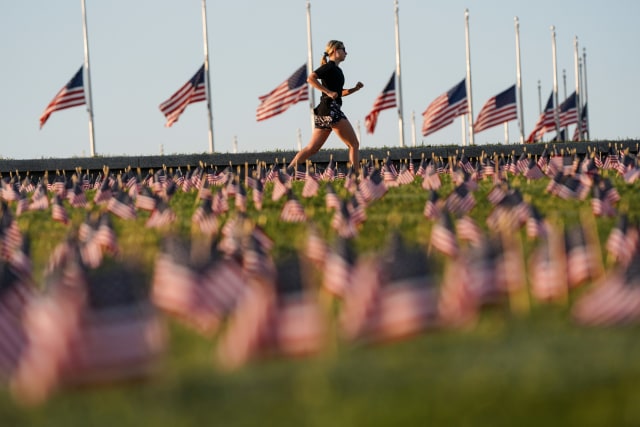 Seorang wanita berlalri melewati bendera Amerika Serikat yang dipasang di tugu peringatan orang-orang yang meninggal karena COVID-19 di National Mall, Washington, Amerika Serikat. Foto: Joshua Roberts/REUTERS