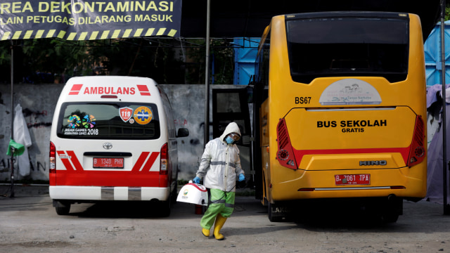 Pekerja mengenakan alat pelindung diri (APD) membawa blower disinfektan saat mebersihkan bus sekolah sebelum mengakngkut pasien corona ke RS Darurat COVID-19 Wisma Atlet di Jakarta.  Foto: Willy Kurniawan/REUTERS