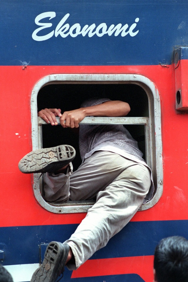 Seorang penumpang menaiki kereta api melalui jendela kereta api di stasiun Pasar Senen, Jakarta pada 17 Januari 1999. Foto: JEWEL SAMAD / AFP