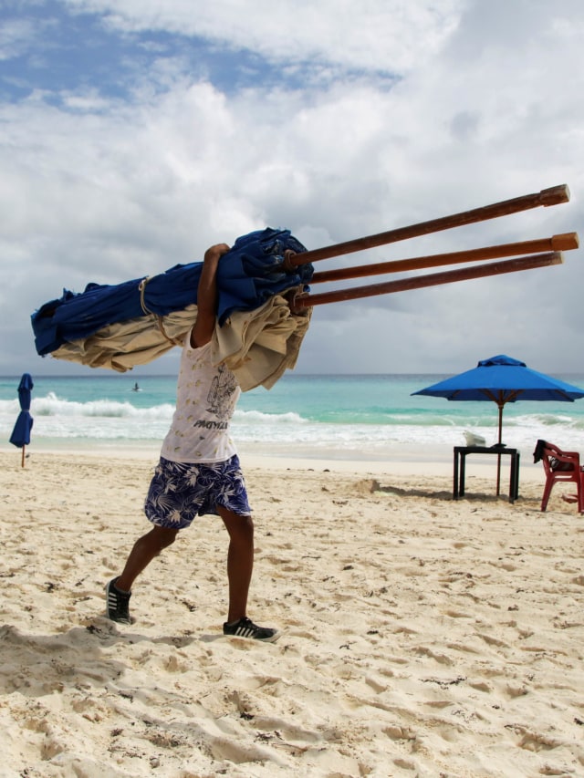 Seorang karyawan hotel melepas payung pantai dari pantai sebagai persiapan untuk kedatangan Badai Delta, di Cancun, Meksiko. Foto: Jorge Delgado/Reuters