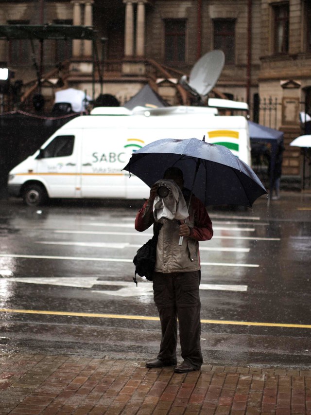 Seorang fotografer memegang payung di bawah guyuran hujan saat ia meliput hari kedua persidangan bintang Paralimpiade Afrika Selatan. Foto: Marco Longari/AFP