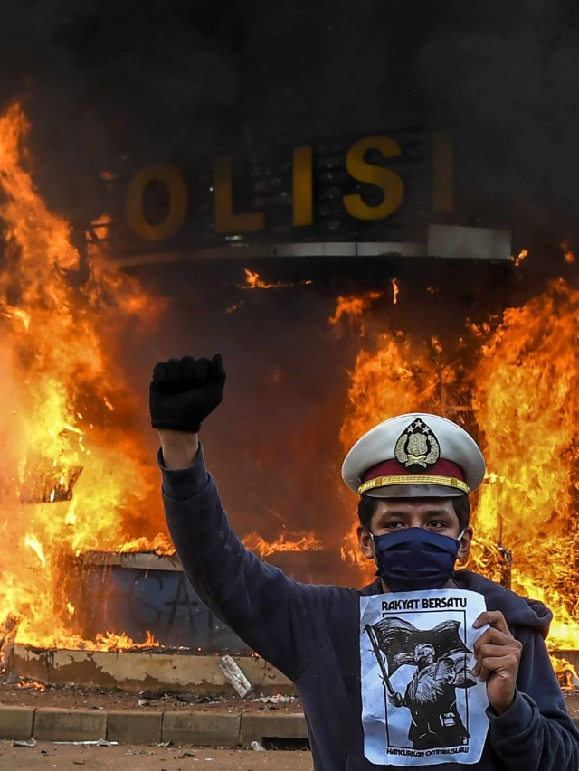 Pengunjuk rasa berfoto dengan latar belakang api yang membakar pos polisi saat demonstrasi menentang UU Cipta Kerja di kawasan Patung Kuda, Jakarta. Foto: Galih Pradipta/Antara Foto