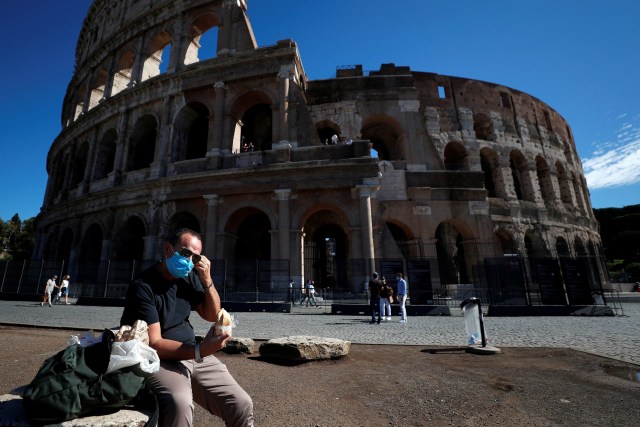 Seseorang bersantai di sekitar Colosseum sambil mengenakan masker. Foto: Guglielmo Mangiapane/Reuters