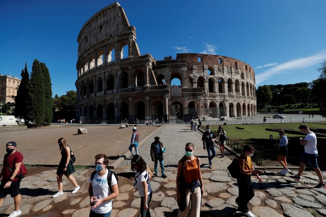 Orang-orang  mengenakan masker berjalan melewati Colosseum ketika otoritas lokal di ibu kota Italia Roma memerintahkan agar penutup wajah dikenakan setiap saat di luar ruangan. Foto: Guglielmo Mangiapane/Reuters