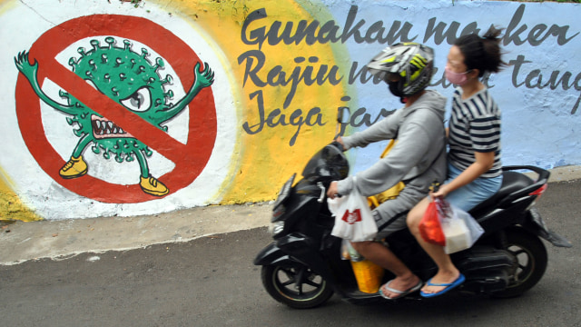 Pengendara motor menggunakan masker melintas disamping mural bergambar protokol kesehatan COVID-19 di jalan Roda 2 Gang Mesin RT 01/01, Kelurahan Babakan Pasar, Kota Bogor, Jawa Barat, Minggu (11/10/2020).  Foto: ARIF FIRMANSYAH/ANTARA FOTO