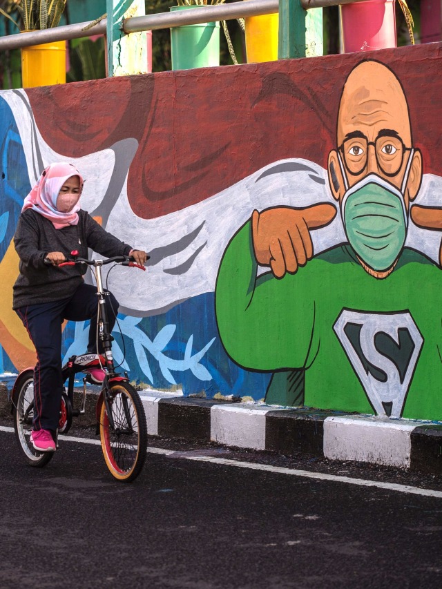 Seorang warga bersepeda melewati mural yang mengajak warga untuk memakai masker di tengah pandemi COVID-19 di Surabaya. Foto: Juni Kriswanto/AFP