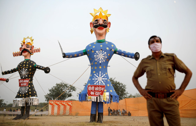 Seorang polisi yang mengenakan masker berdiri di samping iblis Raja Rahwana (kiri) dan saudaranya Kumbhkarana sebelum mereka dibakar selama festival Hindu Dussehra di India, Minggu (25/10). Foto: Adnan Abidi/REUTERS