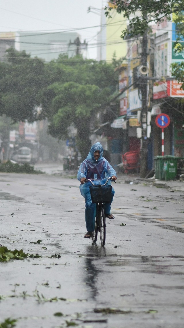 Seorang pria bersepeda di sepanjang jalan sepi di tengah angin kencang di provinsi Quang Ngai, Vietnam, Rabu (28/10). Foto: MANAN VATSYAYANA/AFP