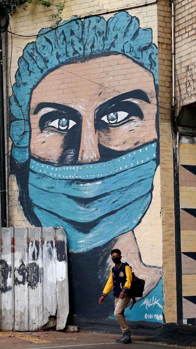 Seorang pria berwajah pelindung berjalan melewati mural yang mempromosikan kesadaran akan virus corona di Jakarta. Foto: Ajeng Dinar Ulfiana/REUTERS 