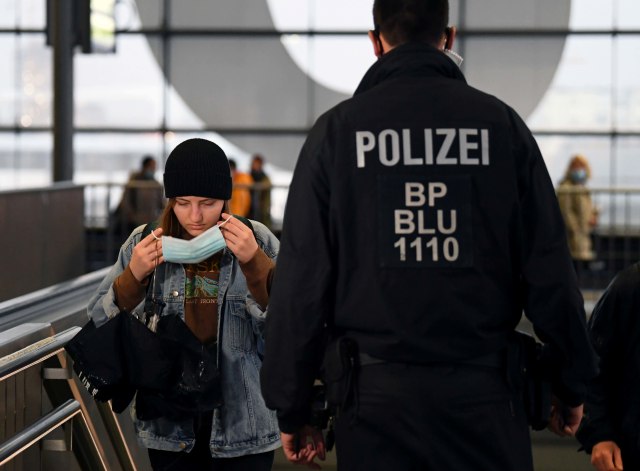 Seorang wanita mengenakan masker di samping petugas polisi yang berjalan di stasiun Ostkreuz, Berlin, Jerman. Foto: Annegret Hilse/Reuters