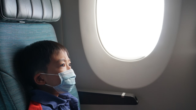 Anak pakai masker naik pesawat saat pandemi. Foto: Shutterstock