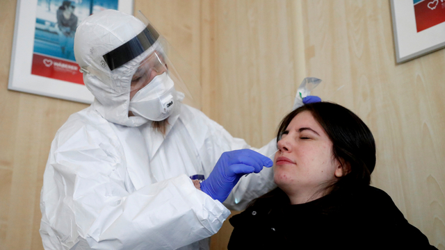 Petugas kesehatan mengumpulkan sampel usap kepada seorang wanita di lokasi pengujian COVID-19 di Budapest, Hungaria. Foto: Bernadett Szabo/REUTERS