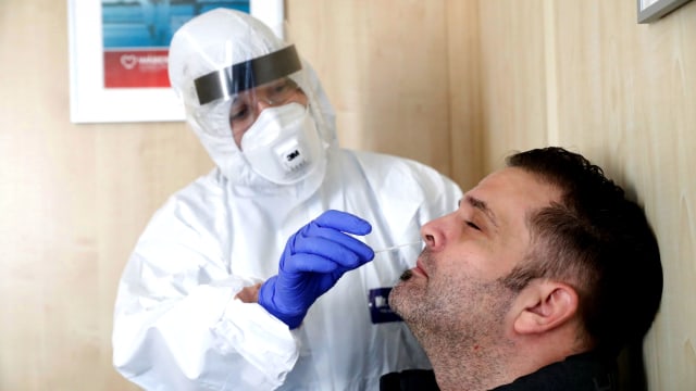 Petugas kesehatan mengumpulkan sampel usap kepada seorang pria di lokasi pengujian COVID-19 di Budapest, Hungaria. Foto: Bernadett Szabo/REUTERS