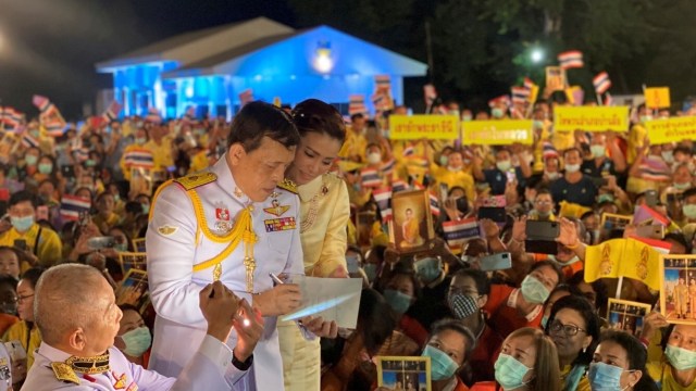Raja Thailand Maha Vajiralongkorn dan Ratu Suthida menulis pesan di atas kertas saat mereka menyapa para demonstran di provinsi Udon Thani, Thailand. Foto: Royal Household Bureau/via REUTERS