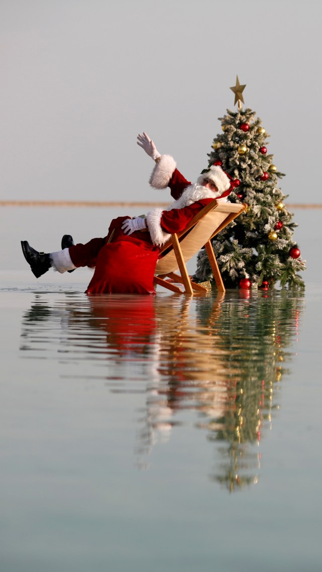 Sinterklas berpose sambil duduk di samping pohon Natal di atas formasi garam di Laut Mati, dekat Ein Bokeq, Israel. Foto: Amir Cohen/REUTERS