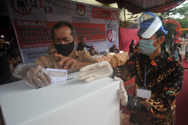 Petugas KPPS mendampingi pemilih yang menggunakan sarung tangan dan masker, memasukan surat suara ke kotak, saat simulasi pemilihan serentak di Padang, Sumatera Barat, Sabtu (21/11). Foto: Iggoy el Fitra/ANTARA FOTO