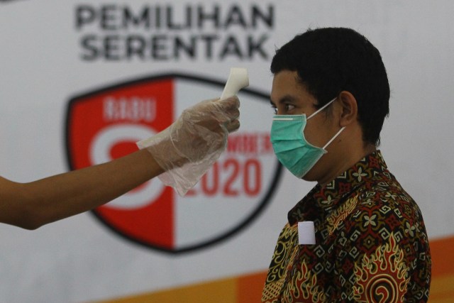Petugas KPPS memeriksa suhu tubuh warga sebelum menggunakan hak pilihnya saat simulasi pemungutan dan penghitungan suara Pilkada 2020, di Kantor KPU Kota Surabaya, Jawa Timur, Sabtu (21/11).  Foto: Moch Asim/ANTARA FOTO