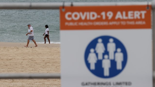 Orang-orang berjalan di tepi laut melampaui tanda peringatan kesehatan masyarakat penyakit coronavirus (COVID-19) di Bondi Beach, di Sydney, Australia, Senin (23/11). Foto: LOREN ELLIOTT/REUTERS