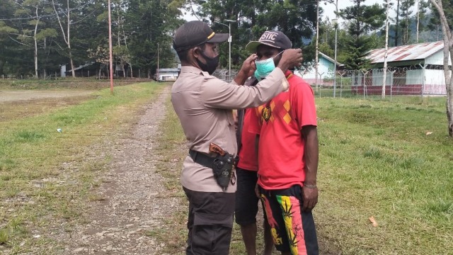 Kapolsek Bokondini, Ipda Remi Kogoya memakaikan masker kepada masyarakat setempat. (Dok Polda Papua)
