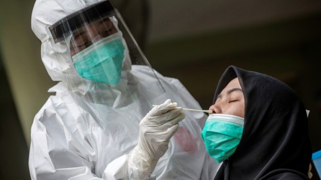 Seorang petugas medis mengambil sampel dari seorang siswa sekolah menengah untuk menguji virus Corona, di Surabaya. Foto: AFP/JUNI KRISWANTO