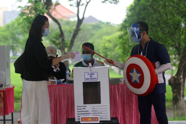 Petugas KPPS berkostum super hero mengarahkan warga untuk memasukkan surat suara ke dalam kotak suara usai mencoblos di TPS 14, Perumahan Citraland, Surabaya. Foto: Moch Asim/Antara Foto