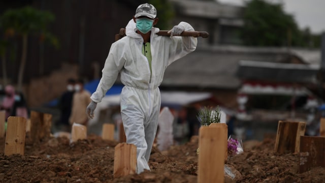 Petugas yang mengenakan APD bersiap memakamkan jenazah dengan protokol COVID-19 di TPU Tegal Alur, Jakarta, Selasa (29/12).  Foto: Wahyu Putro A/ANTARA FOTO