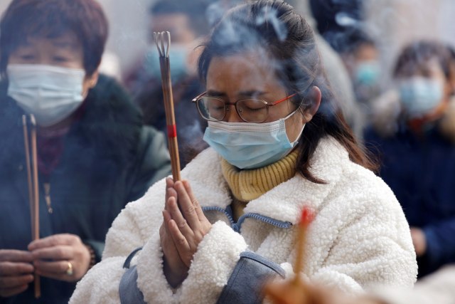 Seorang wanita mengenakan masker memegang dupa saat berdoa di sebuah kuil Buddha pada hari tahun baru 2021 di Wuhan, Hubei, China, Jumat (1/1).  Foto: Tingshu Wang/REUTERS