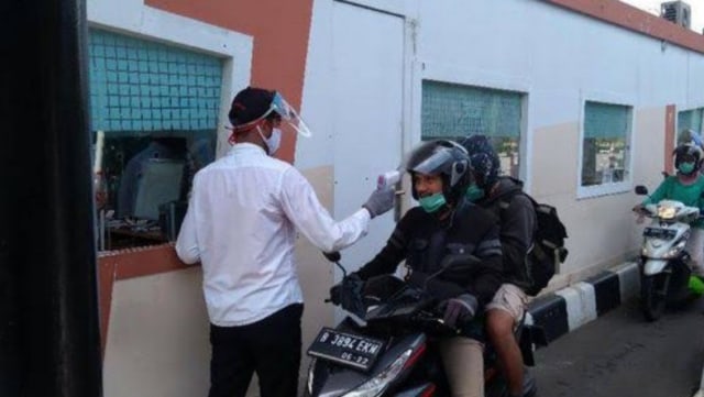 Petugas mengecek suhu tubung pengunjung yang menggunakan sepeda motor di pintu masuk Taman Mini Indonesia Indah (TMII), Jakarta Timur, Minggu (3/1). Foto: Humas TMII/HO/ANTARA