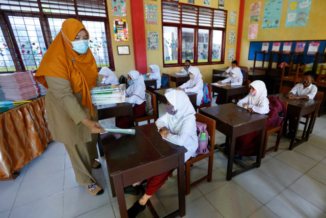 Guru membagikan buku pelajaran kepada pelajar pada hari pertama sekolah tatap muka di SD Negeri 42, Banda Aceh, Aceh, Senin (4/1/2021). Foto: Irwansyah Putra/ANTARA FOTO