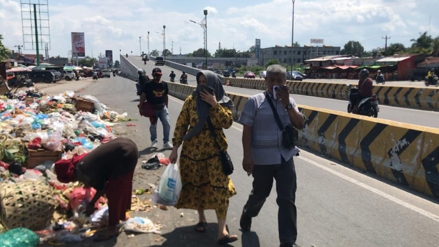 DUA warga menutup hidungnya saat melewati gunungan sampah di TPS Pasar Pagi Arengka/Soekarno-Hatta, Pekanbaru. 