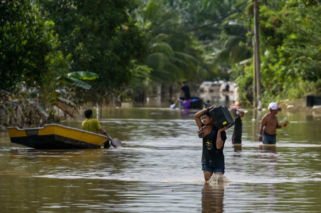 Penduduk berjalan di sepanjang jalan yang terendam banjir di Mentakab di negara bagian Pahang Malaysia, Jumat (8/1/2021). Foto:  Mohd Rasfan/AFP