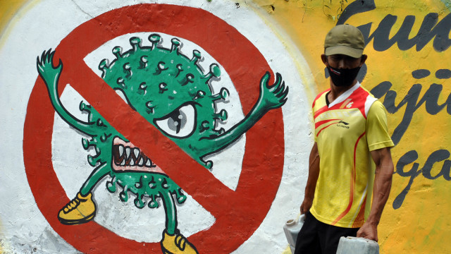 Warga menggunakan masker berjalan di samping mural bergambar COVID-19 di jalan Roda 2 Gang Mesin RT 01/01, Kelurahan Babakan Pasar, Kota Bogor, Jawa Barat. Foto: Arif Firmansyah/ANTARA FOTO