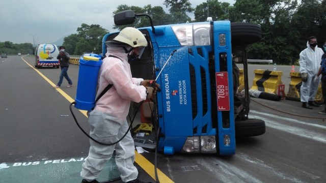 Petugas menyemprot disinfektan di bus pembawa pasien corona yang terguling di Tol Jagorawi. Foto: Dok. Istimewa