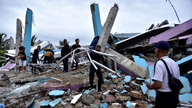 Tim penyelamat mencari korban di sebuah bangunan yang runtuh akibat diguncang gempa di kota Mamuju, Sulawesi Barat, Jumat (15/1). Foto: FIRDAUS/AFP