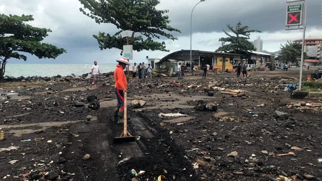 Petugas dari kawasan megamas Manado membersihkan material pasir dan kerikil yang terbawa air laut saat banjir rob terjadi Minggu (17/1). (foto: febry kodongan/manadobacirita)