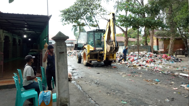 ALAT berat sedang membersihkan dan mengangkut tumpukan sampah yang menggunung di Pasar Palapa, Jalan Durian, Pekanbaru. Di sebelahnya terdapat masjid. 