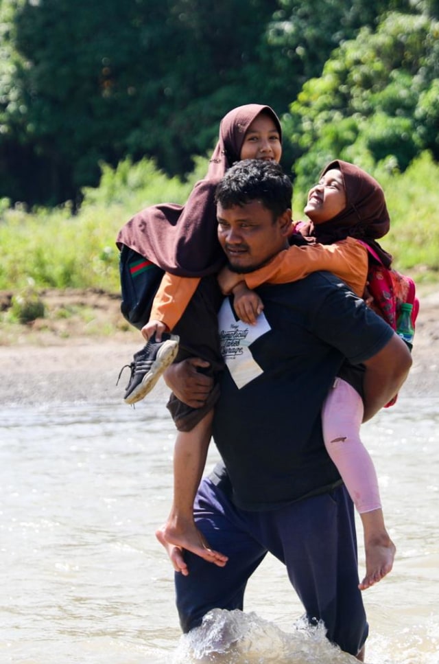 Orang tua menggendong anaknya arungi sungai untuk ke sekolah. Foto: Suparta/acehkini